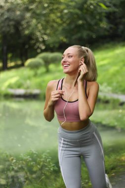 Genç güzel kız parkta koşuyor. Sabah koşusu. Kulaklıkla koşuyor. Motive edici müzik listesi dinliyor..