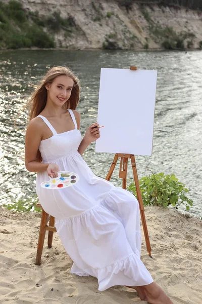 クリエイティブな女性アーティストが 自然の中で新しいアイデアを描くことに取り組んでいます ペイント パレット ブラシで描いています 彼女はイーゼル近くに座っている 彼女は微笑んでいる — ストック写真