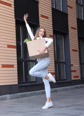 Güzel, genç bir bayan evin dekorasyonu ve apartmanın iç bahçesiyle birlikte kutunun yanında duruyor. Yeni bir eve taşınıyor. O mutlu..