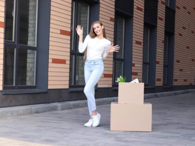Güzel genç bir bayan, apartmanın dışında elinde dekorla kutunun yanında duruyor. Yeni bir eve taşınıyor. O mutlu..