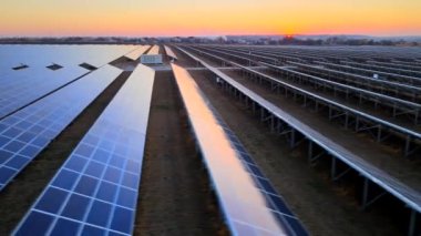 Hava aracı bulutlu bir yaz akşamında güneş çiftliğinin büyük güneş panellerine yakın çekim yapıyor. Güneş pili santralleri, koyu yeşil çimenler. Renkli HDR görüntüsü 4k.