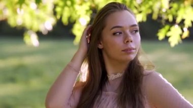 Portrait of beautiful woman posing in the park. Portrait of gentle female person looking at camera with love. Smiling woman face.