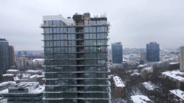 Drone view of industrial climbers in orange uniform and helmets working on high new modern building in European city in snowy winter. Dangerous work, professional climbers, alpinism
