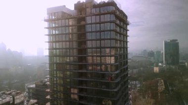 Drone view of industrial climbers in orange uniform and helmets working on high new modern building in European city. Dangerous work, professional climbers, alpinism