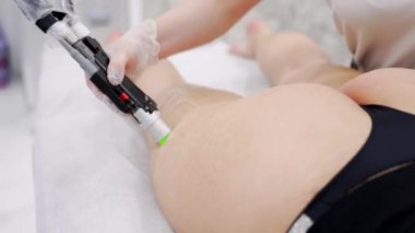 Close up video of professional cosmetologist doing alexandrite laser hair removal of legs to young woman in modern beauty clinic