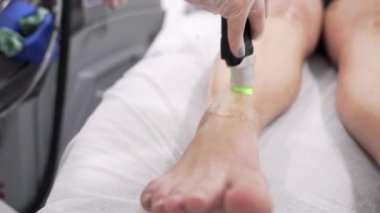 Profesyonel kozmetolojistin, güzellik salonundaki genç bayanın ayaklarına lazer kılı aldırma videosunu kapatın. Güzellik konsepti.