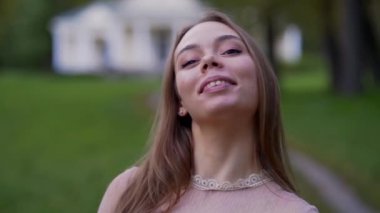 Yavaş çekim videosu. Parkta poz veren güzel bir kadının portresi. Kameraya sevgiyle bakan nazik kadın portresi. Gülümseyen kadın yüzü.