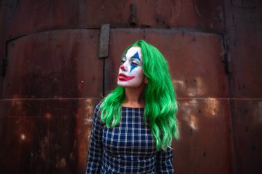 Atmosferik paslı metal arka planda Joker makyajlı, yeşil saçlı bir kızın portresi..