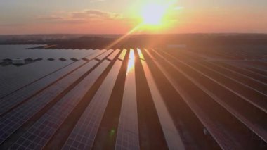 Hava aracı bulutlu bir yaz akşamında güneş çiftliğindeki büyük güneş panellerine bakıyor. Güneş pili santralleri, koyu yeşil çimenler. Renkli HDR görüntüsü 4k.