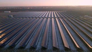 Kışın erken saatlerinde güneş batımında güneş çiftliğindeki büyük güneş panellerinin insansız hava aracı görüntüsü. Güneş pili santralleri. Renkli video 4k.