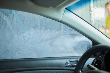 Adam arabasını yıkıyor, otomatik yıkamada pembe aktif köpük kullanıyor, yüksek basınçlı su jeti kullanıyor..