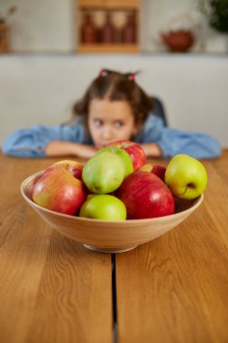 Küçük üzgün kız evdeki meyveli kaseye, sağlıklı çocuk atıştırmalıklarına, evde sağlıklı yiyeceklere, meyve ve vitaminlere bakar..