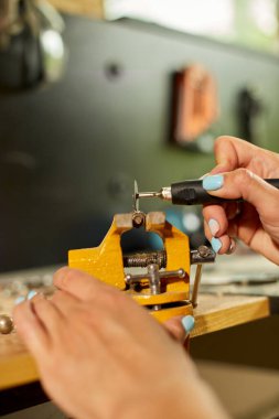 Çalışan bir kadın öğütücü kullanıyor, kadın eli metal bir fındık öğütüyor, atölyede cıvatalar, metal işçiliğinde kıvılcımlar...