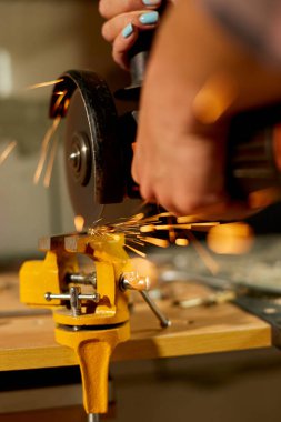 Kadın çilingir, öğütücü makinesiyle çalışır, parlak kıvılcımlar saçar. Dişi bir el atölyede metal öğütür, metal işçiliğinde kıvılcımlar saçar..