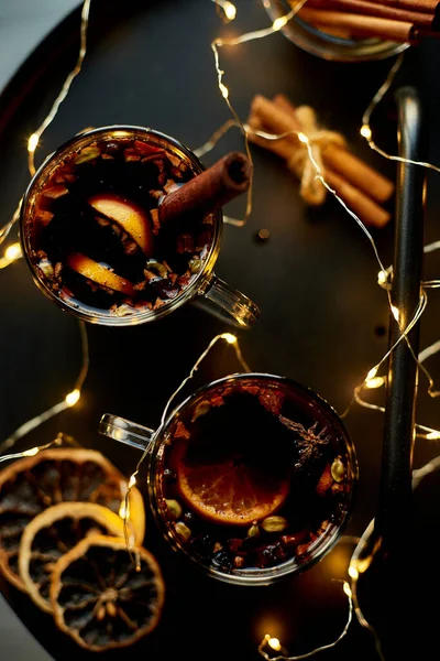 stock image Christmas mulled red wine with spices and oranges on a black table with light garland, traditional hot drink at Christmas, festive cocktail