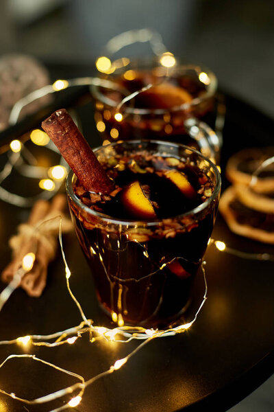Christmas mulled red wine with spices and oranges on a black table with light garland, traditional hot drink at Christmas, festive cocktail