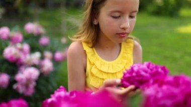 Bahçedeki küçük kız şakayık çalılarında, çocuk çiçeği kokla. Bahçede bir yaz akşamı. Köyde tatil..