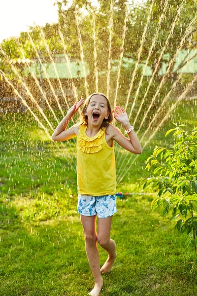 Glückliches Mädchen Das Mit Sprinklerlauf Und Springen Garten Spielt Sommerlicher lizenzfreie Stockbilder