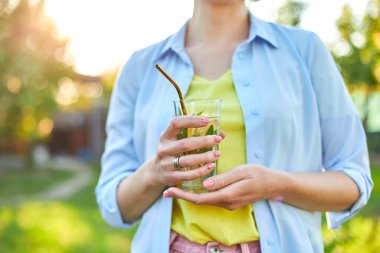 Yaz narencili limonata içen bir kadın soğuk içecek, yaz mevsimi, çevre dostu içecek pipetli, sağlıklı yaşam tarzı, vejetaryen yemeği, detoks suyu olan bir arka bahçe evinde yeniden kullanılabilir metal pipetlerle parti veriyor.