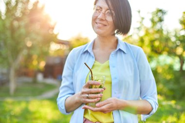 Yaz narencili limonata içen bir kadın soğuk içecek, yaz mevsimi, çevre dostu içecek pipetli, sağlıklı yaşam tarzı, vejetaryen yemeği, detoks suyu olan bir arka bahçe evinde yeniden kullanılabilir metal pipetlerle parti veriyor.