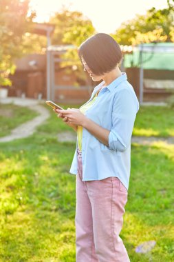 Gözlüklü bir kadın akıllı telefon kullanıyor, cep telefonuna dışarıda mesajlar yazıyor, evde aletlerle boş zaman geçirme kavramı var..