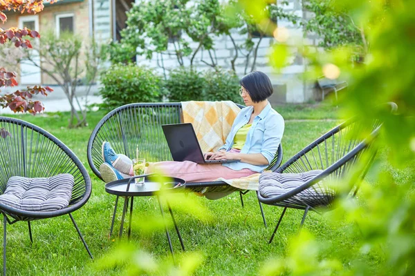 Female typing on the laptop for remote working, Freelancer woman working with laptop, checking social media, shopping online, ordering delivery at home in the backyard outdoor in the garden