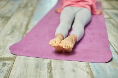 Ayaklarını kapat küçük kız esneme egzersizleri yapıyor, evde yoga yapıyor spor yapıyor, sağlıklı yaşam tarzı uyguluyor. Çocuklar ev karantinası yapıyor