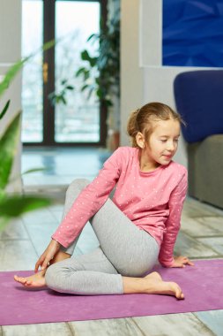 Küçük kız esneme egzersizleri yapıyor, evde fitness minderinde yoga yapıyor spor yapıyor, sağlıklı bir yaşam tarzı sergiliyor. Çocuklar ev karantinası yapıyor
