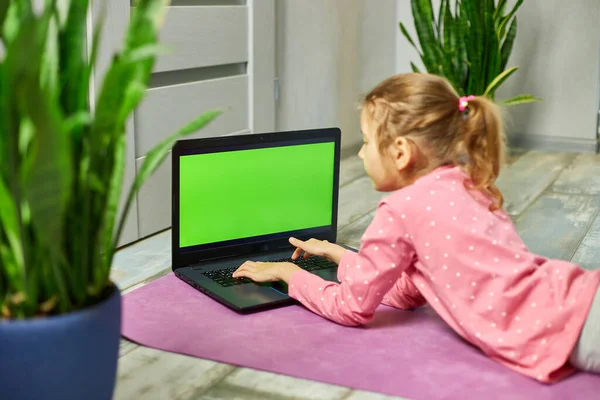 Little girl watching online video on laptop green screen and doing stretching, fitness exercises at home. Child distant training with personal trainer, online education concept, Playing sports, Healthy lifestyle.