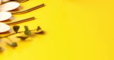 Rotation of reusable stainless steel straws and eco wooden spoons with green leaves on yellow background, eco friendly lifestyle and zero waste concept. Top view, copy space.