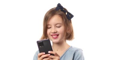 Smiling little girl in casual denim dress hold smartphone, using mobile cell phone internet applications, typing message isolated on white background, studio. Child and modern tech usage concept