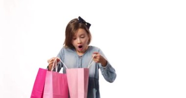 Pretty child girl in casual denim dress hold in hand pink shopping bags on white background, studio, Shopaholic shopping and fashion, discount sale concept, copy space, banner. Black friday