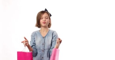Pretty child girl in casual denim dress hold in hand pink shopping bags on white background, studio, Shopaholic shopping and fashion, discount sale concept, copy space, banner. Black friday