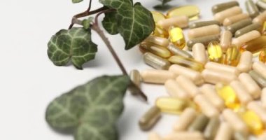 Rotation of Pills, medical tablets with green plants, leaves on white background, Natural herbal medicine concept, Vitamins and omega oils for vegans