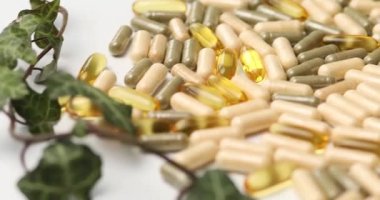 Rotation of Pills, medical tablets with green plants, leaves on white background, Natural herbal medicine concept, Vitamins and omega oils for vegans