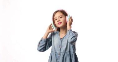 Girl teenager in casual denim dress listening to music in headphones on white background, wireless earphones enjoying music dancing , Modern technology, Protect Developing Ears