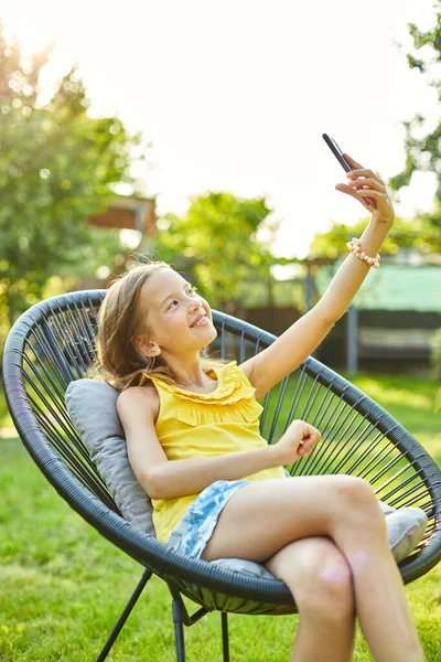 Happy kid girl take selfie on mobile phone in the park outdoor, child using smartphone to take photo at home garden, backyard, sunlight