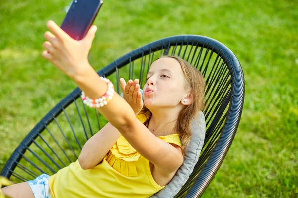 Happy kid girl take selfie on mobile phone in the park outdoor, child using smartphone to take photo at home garden, backyard, sunlight