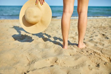 Woman hold in hand straw hat on yhe beach near sea, Summer vacation and travel. Copy space