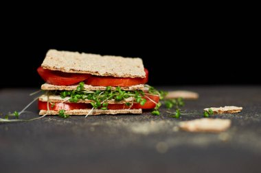 Sağlıklı vejetaryen sandviçi, kıtır çavdar ekmeği domates ve koyu arka planda mikro yeşillikler, diyet gıdalar..