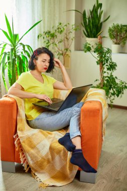 Kadın klavyede daktilo kullanıyor, çalışıyor, e-posta yazıyor, serbest çalışıyor evde defter üzerinde çalışıyor turuncu koltukta yeşil evde oturuyor..