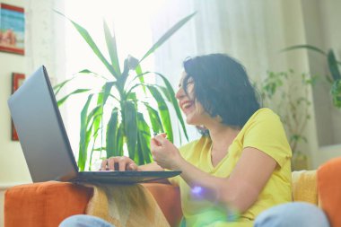 Bilgisayardan video izleyen olumlu kadın ve şakadan kahkaha, çok duygusal bayan, mutlu, yeşil ev, biyofili tasarımı.