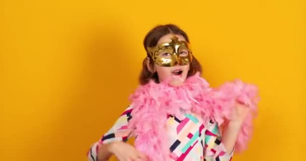 カラフルなブラジルのカーニバルマスクを身に着けている楽しい10代の女の子 ポーズ 黄色のスタジオの背景で楽しみを持っています お祝いの準備ができて 誕生日パーティー 休日のコンセプト — ストック動画