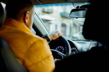 Erkek sürücü, konsantre sakallı, sıradan kıyafetler giyen, modern araba kullanan.