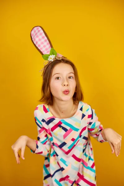 stock image Happy playful teenager girl wearing bunny ears on a bright yellow studio background, celebrating Easter in style.