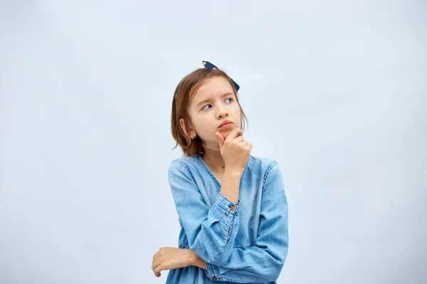 Thoughtful teen girl child wearing jeans dress with finger thinking or considering, have an idea in studio on white background, making decision imagining, idea posing.