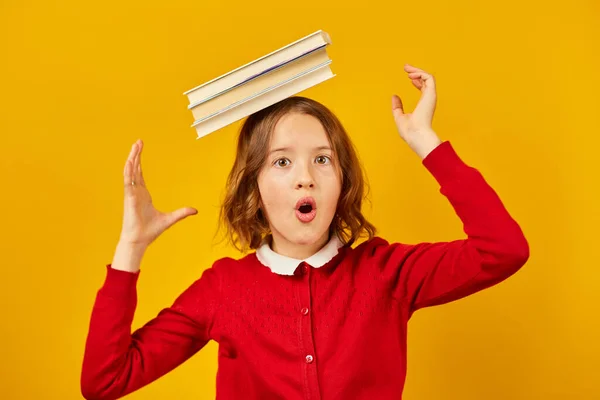 stock image Portrait of happy teenage schoolgirl in uniform holding books on head on yellow studio background, having fun holiday, Back to School concept.