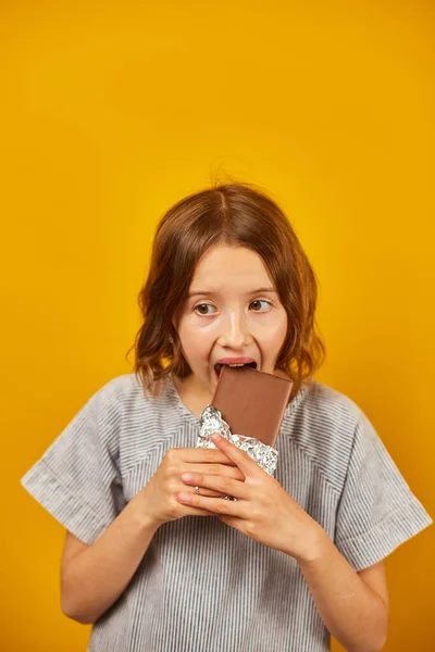 Mooie Tiener Meisje Met Een Chocolade Bar Geïsoleerd Studio Gele — Stockfoto