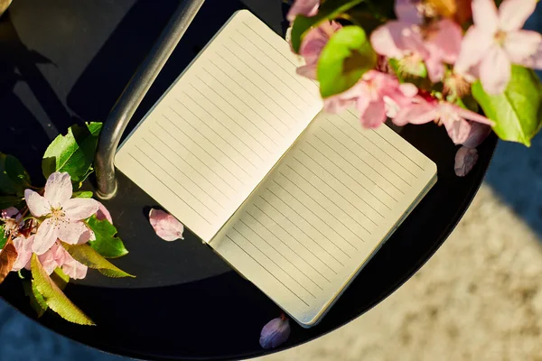 Open notebook and flowers and on the small black table on terrace at home in a sunny day, hardlight, outdoor workspace, summer relaxation, notes, ideas, plannin