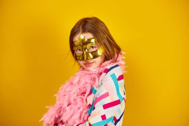 A joyful teenager girl wearing a colorful Brazil carnival mask, posing on yellow studio background, ready for celebration, birthday party, holidays concept